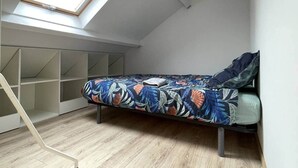 A loft bedroom with a skylight, a bed with a floral bedspread, and built-in shelving. - Cosy downtown studio - ideal location (Challans)