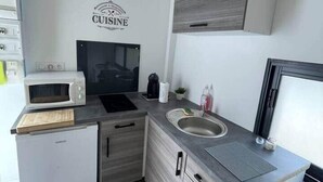 A compact kitchen with a microwave, stove, sink, and a small refrigerator. - Cosy downtown studio - ideal location (Challans)