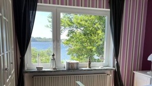 A bedroom with a large window, a radiator, and a view of a tree and water. - Dream View Comfortable Holiday Residence (Maasholm)