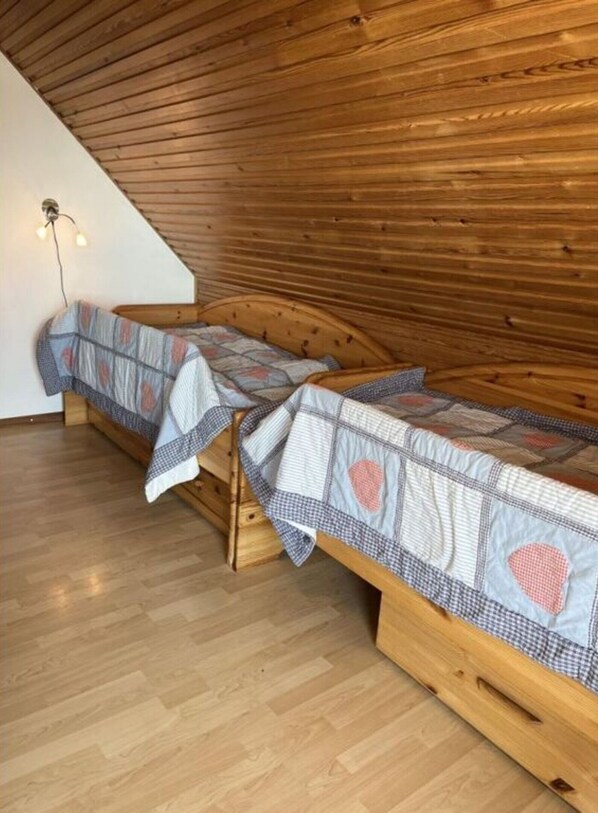 Ett rum med två våningssängar i trä, ett sluttande tak och en lampa på väggen.