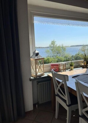 En balkong med utsikt över en sjö, ett bord med stolar och en krukväxt.