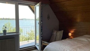 A bedroom with a large bed, a view of a lake through an open door, and a wooden ceiling. - Dream View Comfortable Holiday Residence (Maasholm)