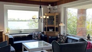 A living room with a sofa set, a coffee table, and a chandelier. There is a window with a view of greenery and a brick wall. - Dream View Comfortable Holiday Residence (Maasholm)