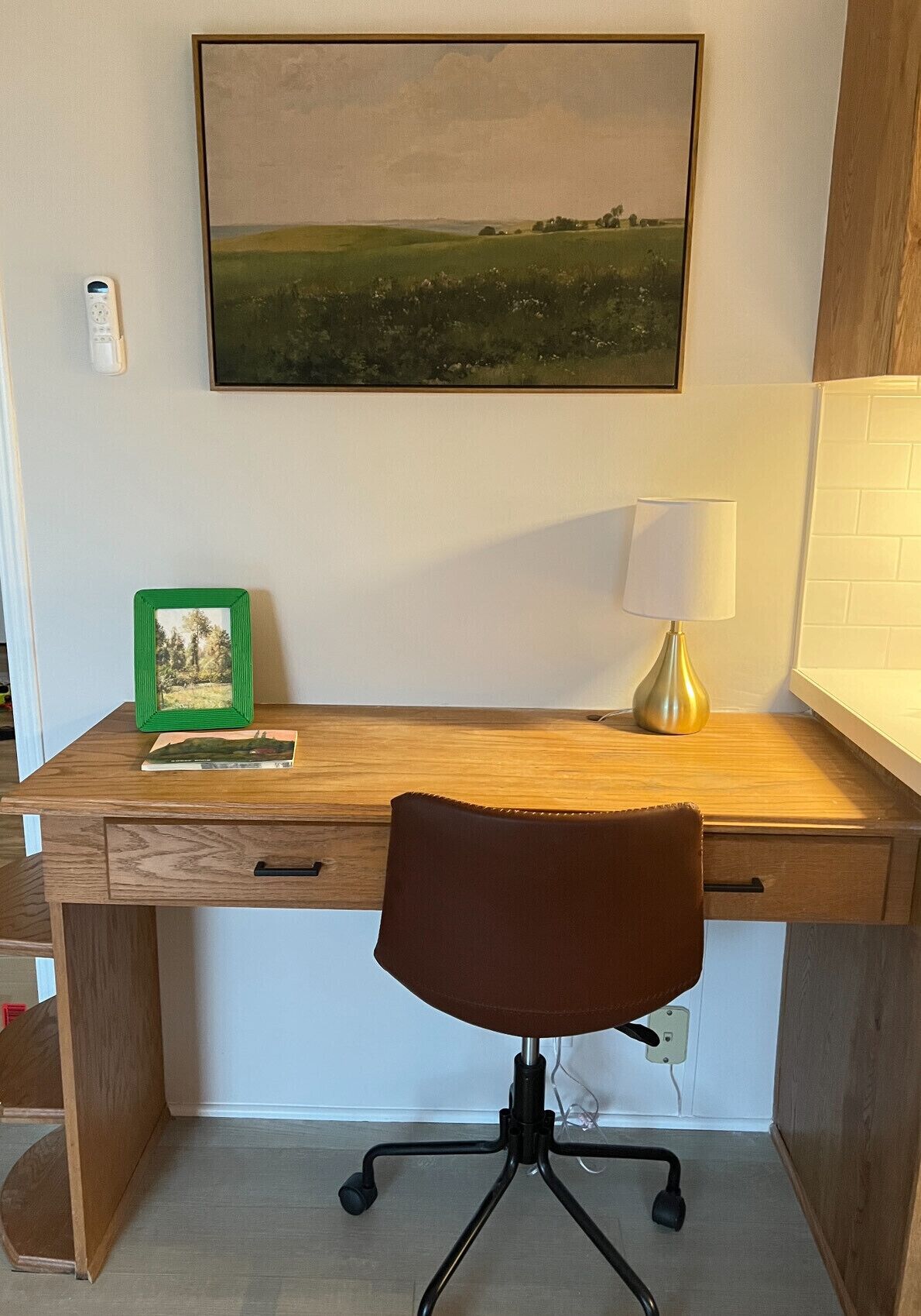 A wooden desk with a brown office chair, a framed picture, and a lamp.