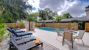 A backyard with a swimming pool, lounge chairs, and a wooden deck.