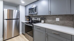 Une cuisine moderne avec des meubles gris, des appareils en acier inoxydable et un plan de travail blanc.