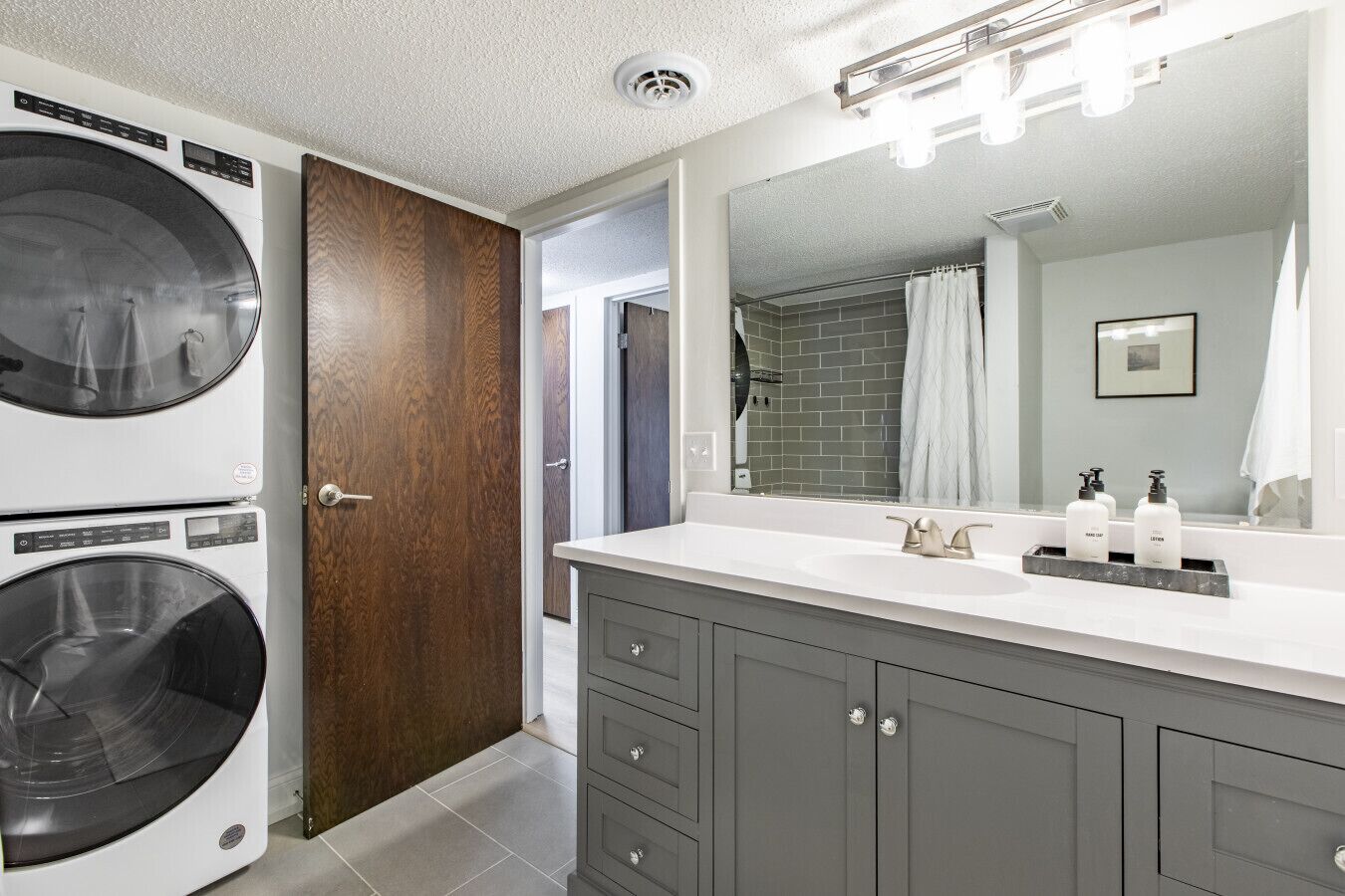 Une salle de bain moderne avec un grand miroir, un lavabo orné de deux flacons de lotion et un lave-linge.