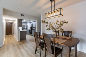 Une cuisine moderne dotée d’appareils électroménagers en acier inoxydable, un coin repas avec une table et des chaises en bois, et un luminaire suspendu.