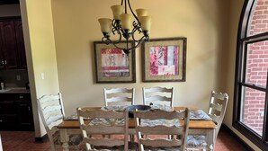 Un coin repas avec une table et des chaises en bois, un lustre et deux œuvres d’art encadrées accrochées au mur.