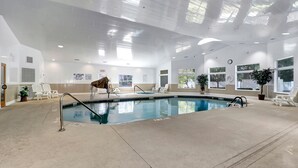 Une piscine intérieure à l’eau claire, entourée de chaises longues blanches et de plantes en pot.