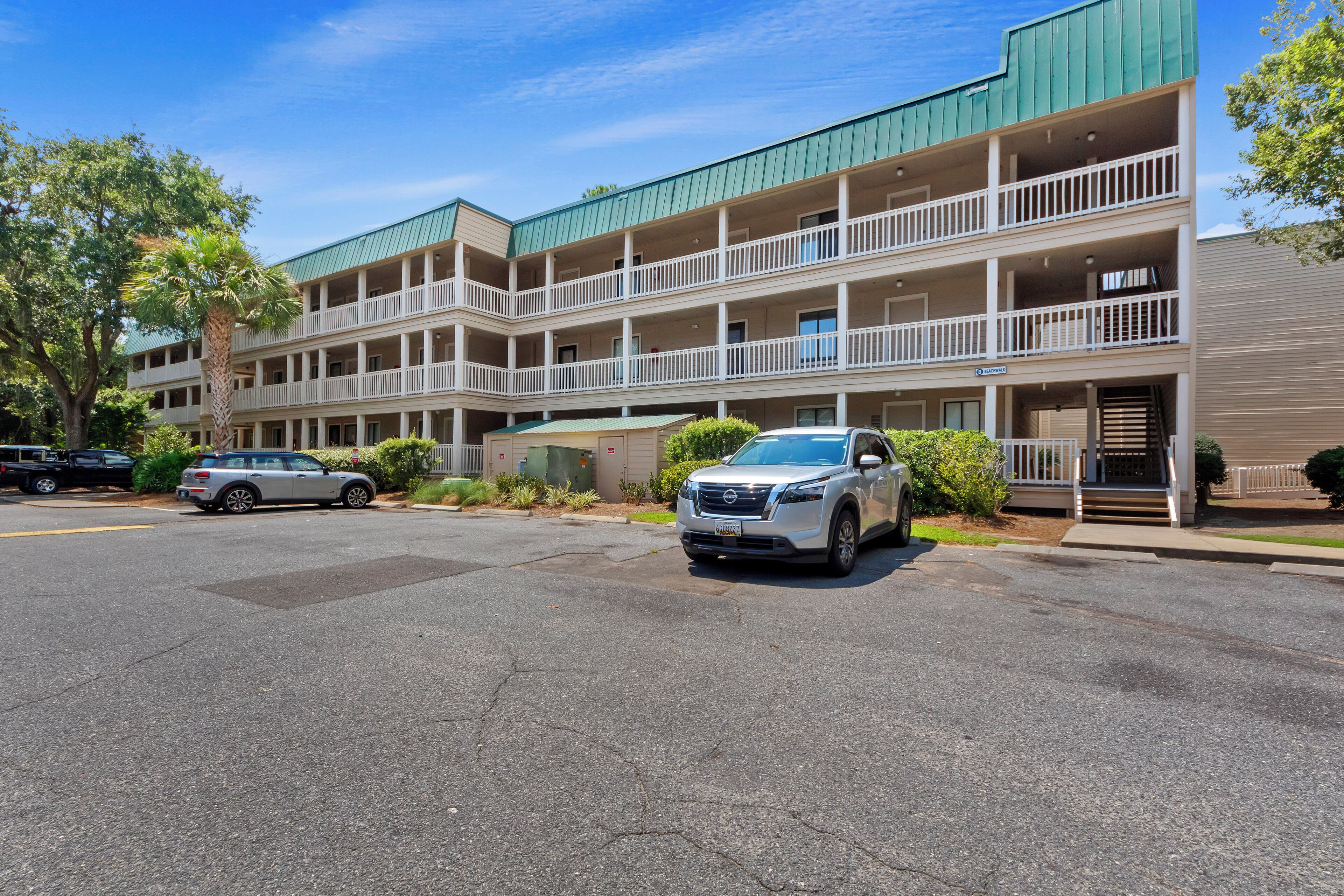 A multi-story hotel with a green roof, balconies, and a parking lot with two cars.