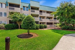 Um edifício residencial de vários andares com varandas, um gramado bem cuidado e árvores já adultas.
