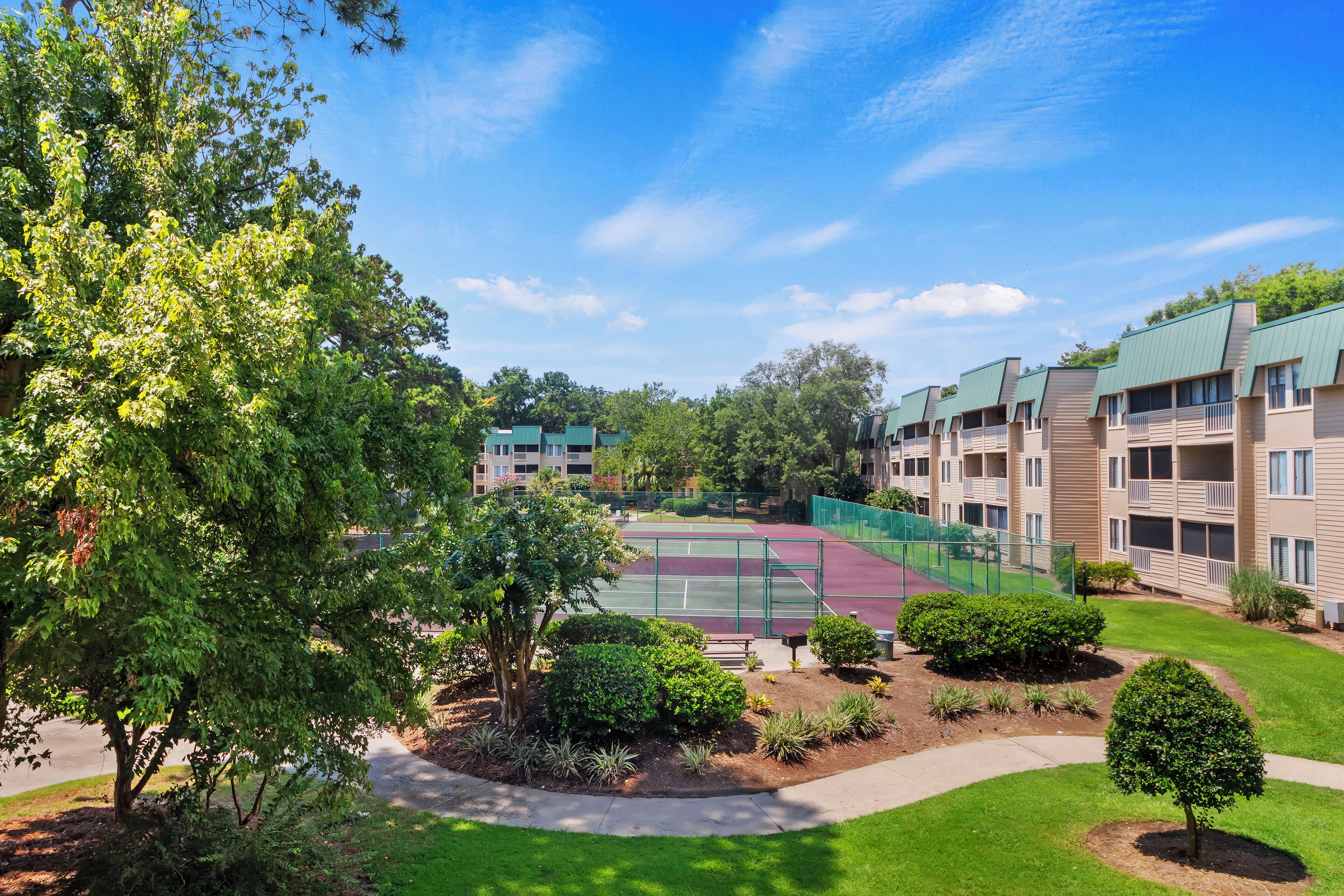A tennis court surrounded by well-maintained landscaping and a multi-story building with balconies.