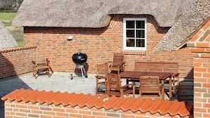 A brick patio with a table and chairs, a grill, and a thatched roof structure. - 4 Star Holiday Home in Ulfborg (Ulfborg)