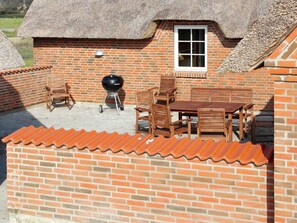 A brick patio with a table and chairs, a grill, and a thatched roof structure. - 4 Star Holiday Home in Ulfborg (Ulfborg)