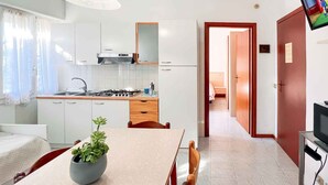 A modern kitchen with white cabinets, a gas stove, and a dining area with a table and chairs. - Holiday flat with air conditioning (Bibione)