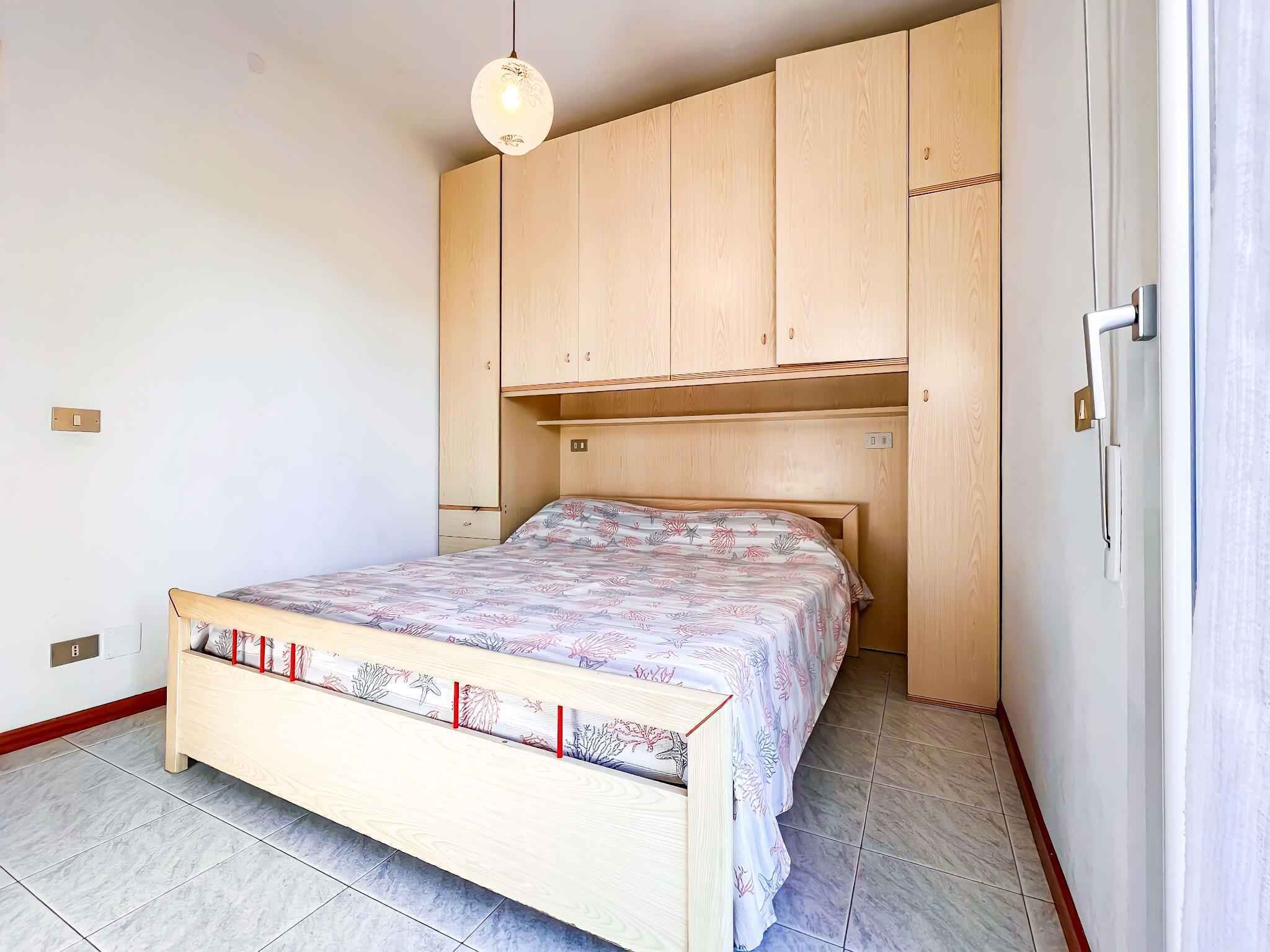 A bedroom with a bed, wooden wardrobe, and a hanging light fixture.