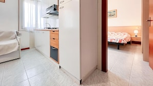 A compact room with a kitchenette, a bed, and a bedside table with a lamp. - Holiday flat with air conditioning (Bibione)