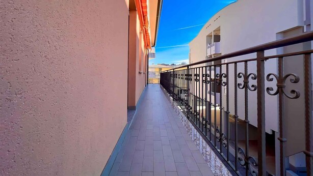 A narrow corridor with a tiled floor, a metal railing, and a building with a beige wall on one side and a white wall on the other. - Holiday flat with air conditioning (Bibione)