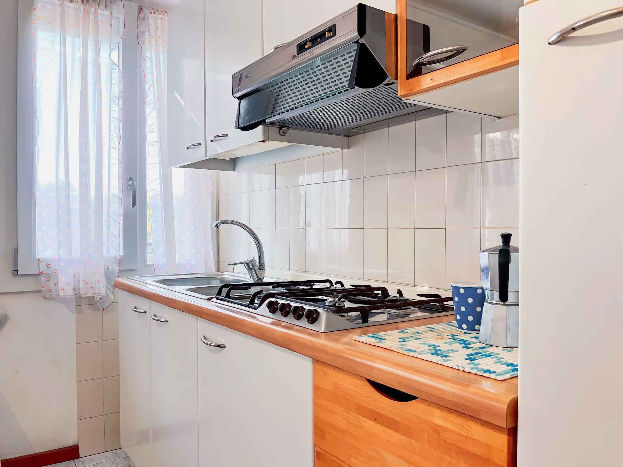 A kitchen with white cabinets, a gas stove, a sink, and a window with floral curtains.