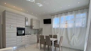 Una cocina moderna con zona de comedor, televisor de pantalla plana y un amplio ventanal con cortinas.
