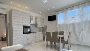 Una sala de estar moderna con sofá, un comedor con sillas, una cocina con armarios y un televisor montado en la pared.
