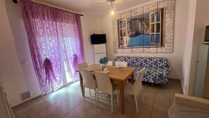 A dining area with a table, chairs, a sofa, and a window with a view of a cliff and water. - Holiday apartment with air conditioning (San Michele al Tagliamento)