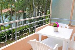 Ein Balkon mit einem weißen Tisch und Stühlen, einem Blumentopf und Blick auf Bäume und Gebäude.