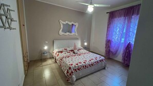 A bedroom with a bed, a ceiling fan, a nightstand, a mirror, and a window with curtains. - Holiday apartment with air conditioning (San Michele al Tagliamento)