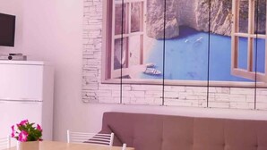 Ein modernes Wohnzimmer mit Steinwand, großem Fenster mit Blick auf die Küste, einer Couch, einem Esstisch mit Stühlen und einem Deckenventilator.