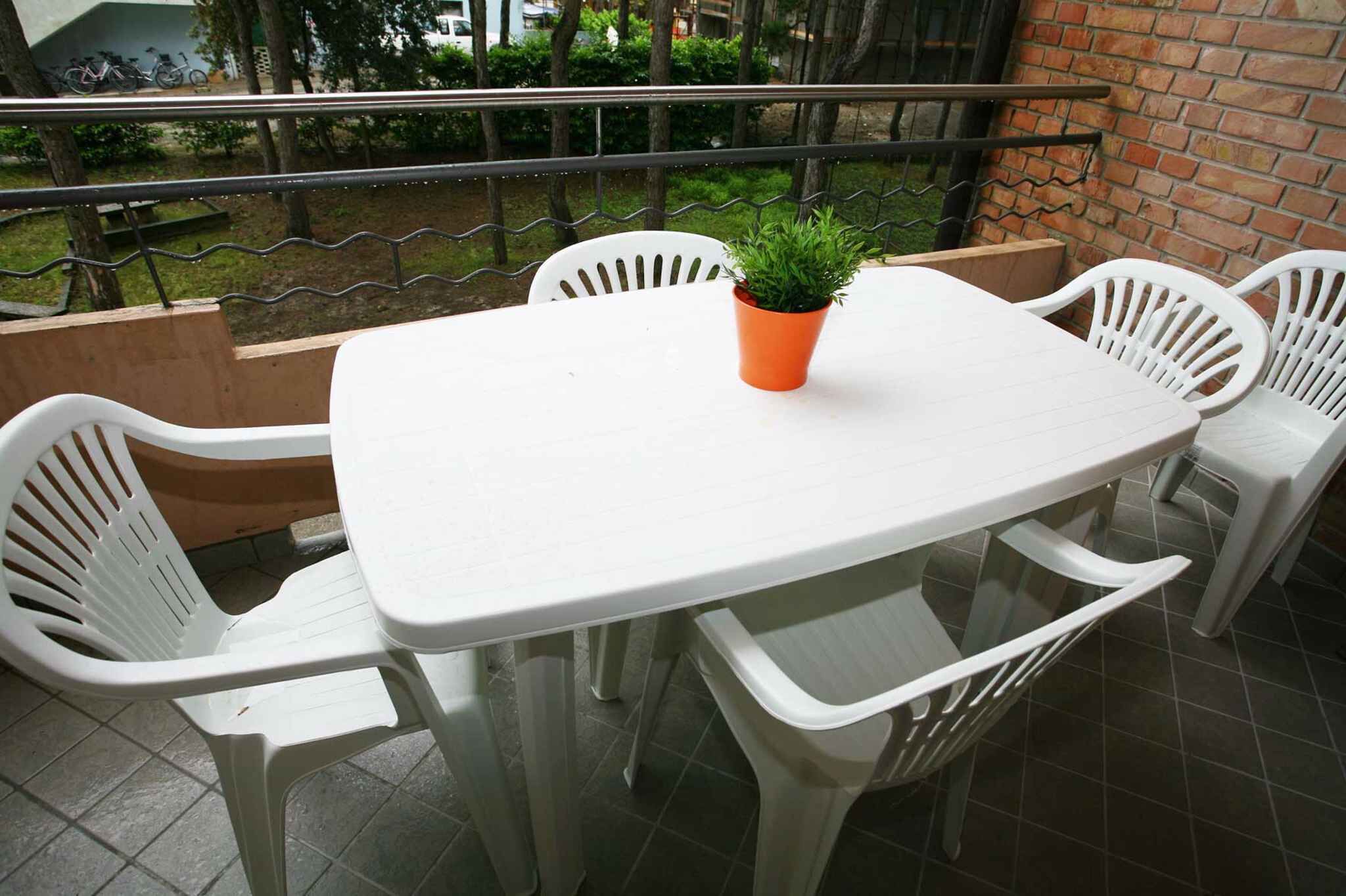 Een witte plastic tafel met vier witte plastic stoelen, een bloempot en een bakstenen muur op de achtergrond.