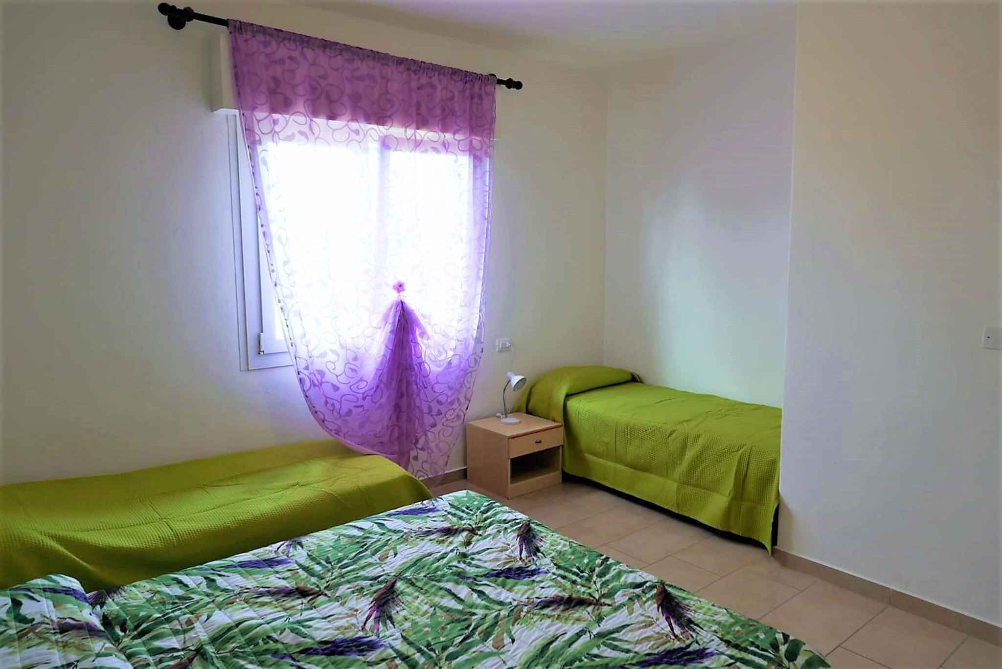 A room with two single beds, a small bedside table, and a window with purple curtains.