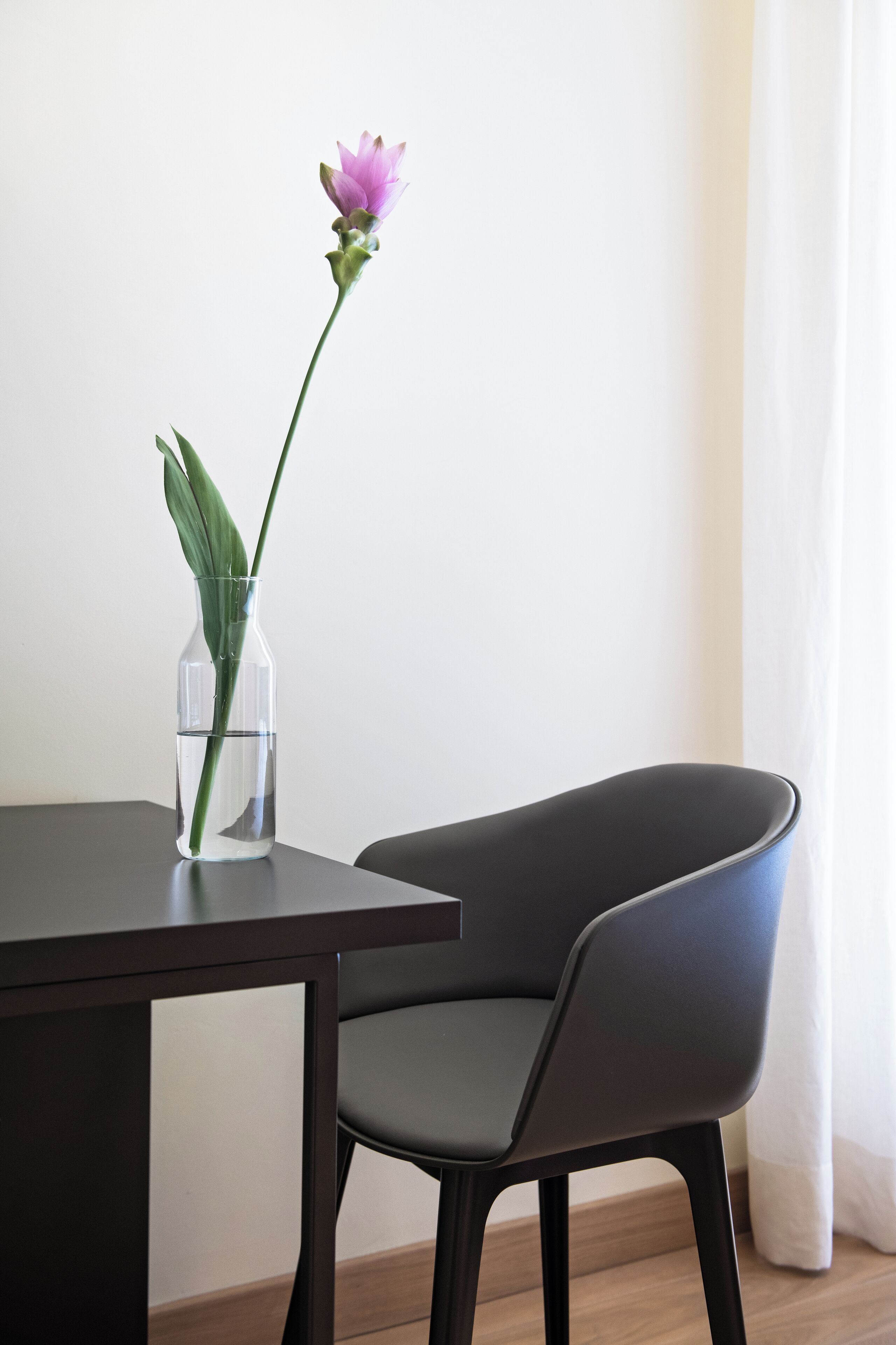 Un vase transparent contenant une seule fleur, posé sur une table à côté d’une chaise.