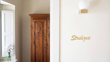A hallway with a wooden wardrobe, a white wall with a gold sign, and a window with a vase of flowers.