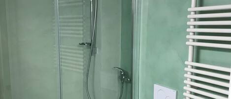 Et badeværelse med en glasafskærmet brusekabine, et hvidt toilet og en hvid vask.