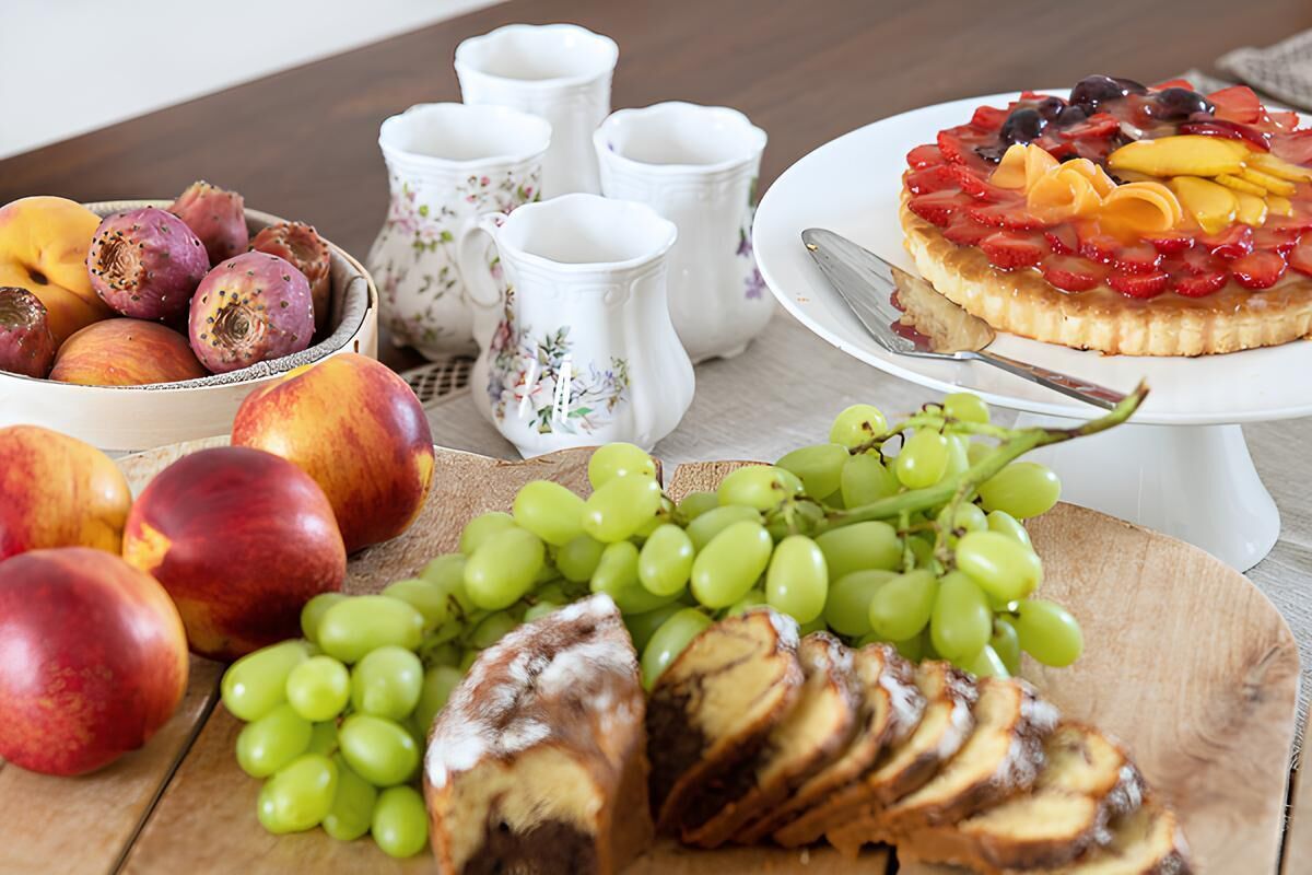 A table with a fruit bowl, a plate of sliced bread, and a fruit tart.