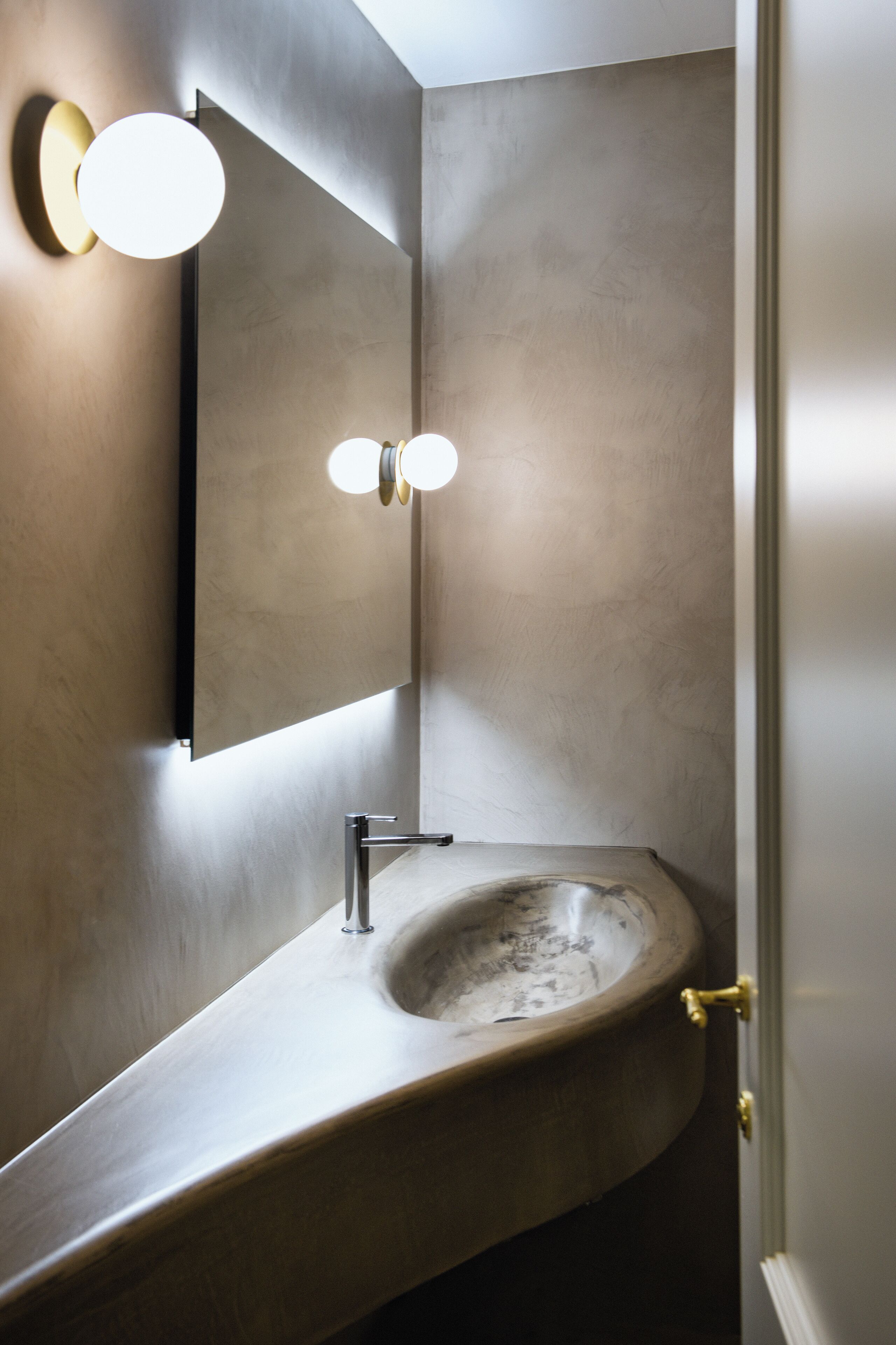 Ein modernes Badezimmer mit einem gewölbten Waschbecken, einem wandmontierten Spiegel und einer Leuchte darüber.