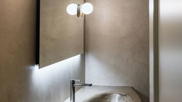 Ein modernes Badezimmer mit einem gewölbten Waschbecken, einem wandmontierten Spiegel und einer Leuchte darüber.
