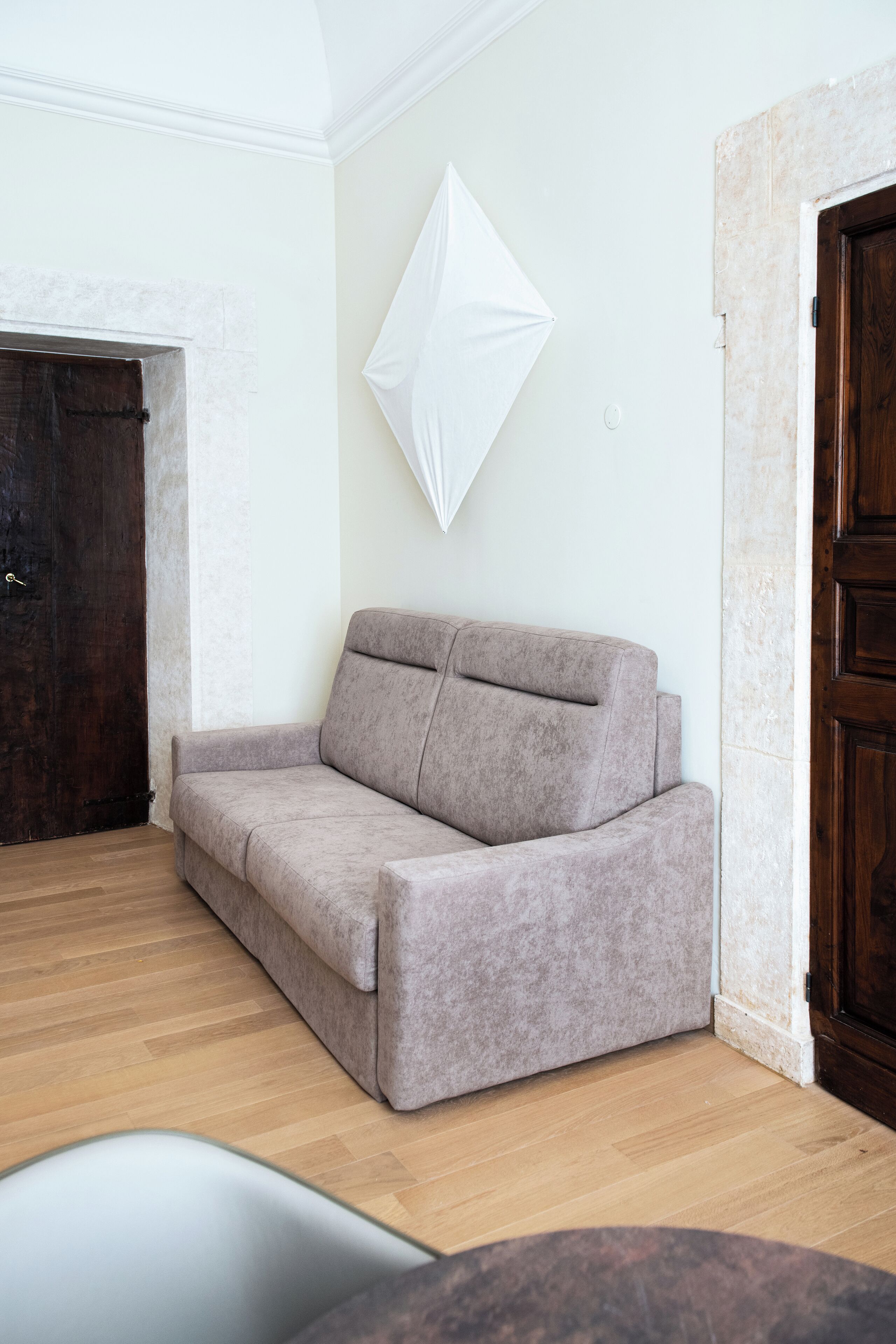 Une pièce avec un canapé de couleur claire, une porte en bois et un mur blanc.