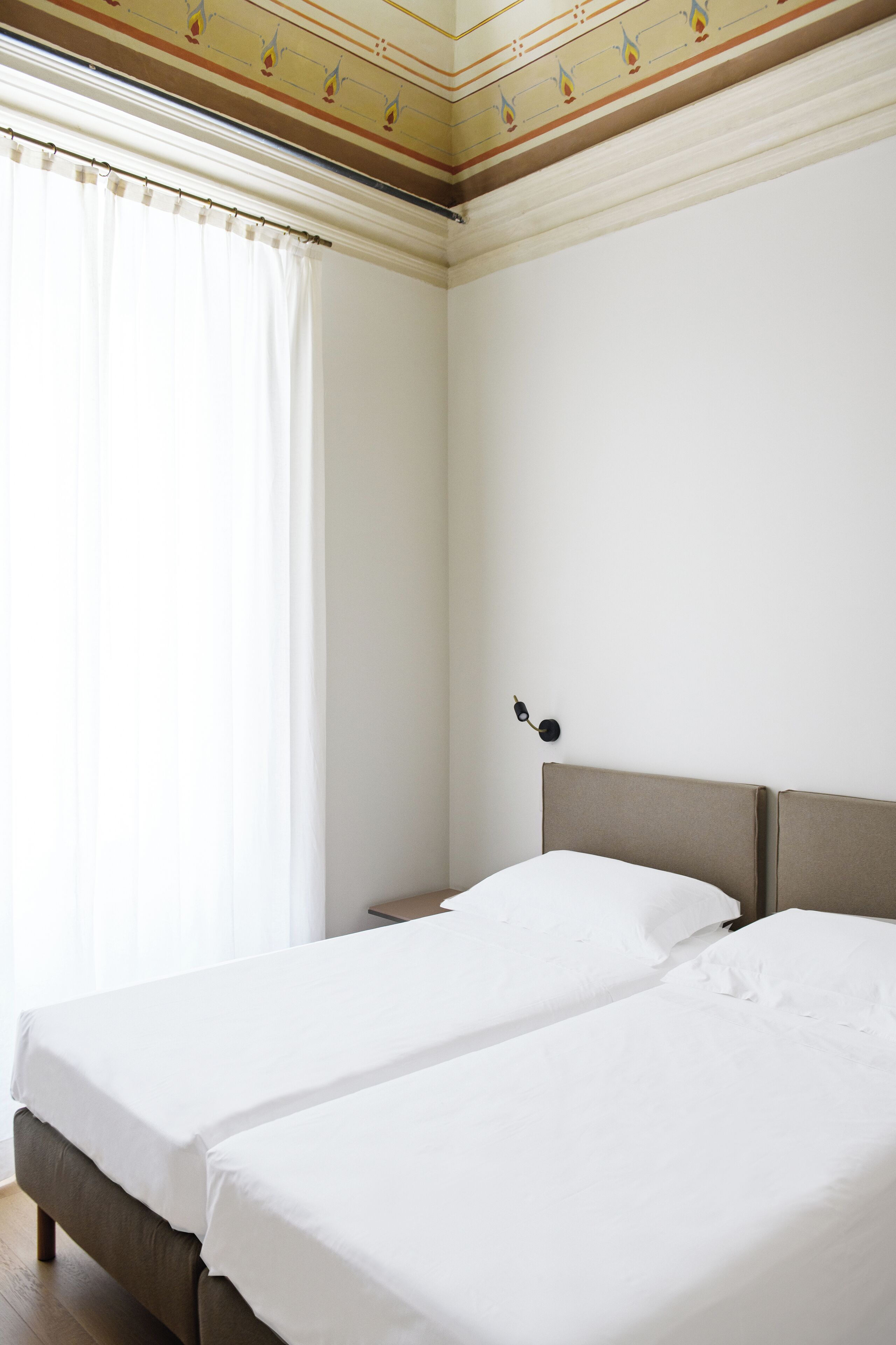 Une chambre avec deux lits, une fenêtre avec des rideaux et un luminaire fixé au mur.