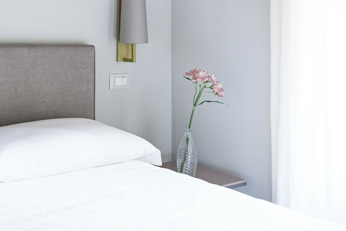 A hotel room with a bed, a nightstand, a lamp, and a vase with flowers.
