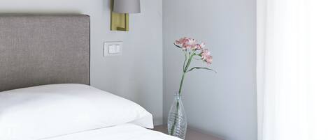 A hotel room with a bed, a nightstand, a lamp, and a vase with flowers.