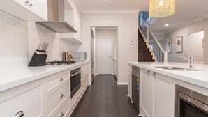 Una cocina moderna con armarios blancos, estufa a gas y pileta de acero inoxidable.