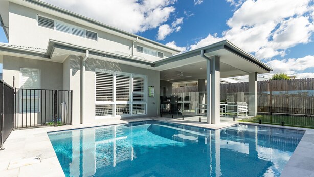 Una casa moderna con piscina, patio cubierto y patio trasero cercado.
