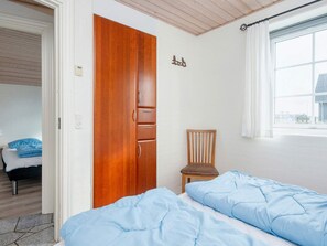 A bedroom with a bed, a wooden wardrobe, a chair, and a window with curtains. - 4 Star Holiday Home in Harboore (Harboore)