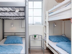 Un dormitorio con literas, un pequeño estante metálico con una planta y una ventana con vistas.
