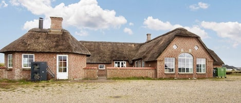 A traditional brick building with a thatched roof, a gravel driveway, and a clear sky.