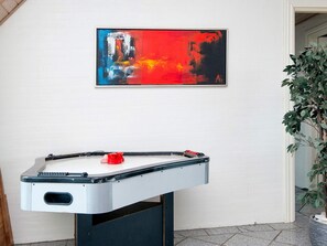 Una mesa de futbolín en una habitación con pared blanca y un cuadro abstracto enmarcado encima.