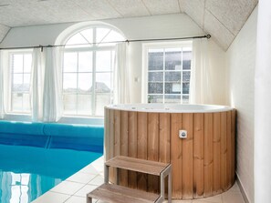 A hot tub with a wooden exterior, a small wooden step, and a pool with clear blue water. - 4 Star Holiday Home in Harboore (Harboore)