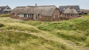 A traditional thatched-roof house with a brick exterior, a wooden bench, and a grassy landscape. - 4 Star Holiday Home in Harboore (Harboore)